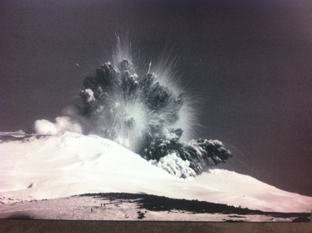 Explosive Mount Ruapehu volcanic eruption from a snow-covered mountain, with a large dark ash cloud rising above the summit.