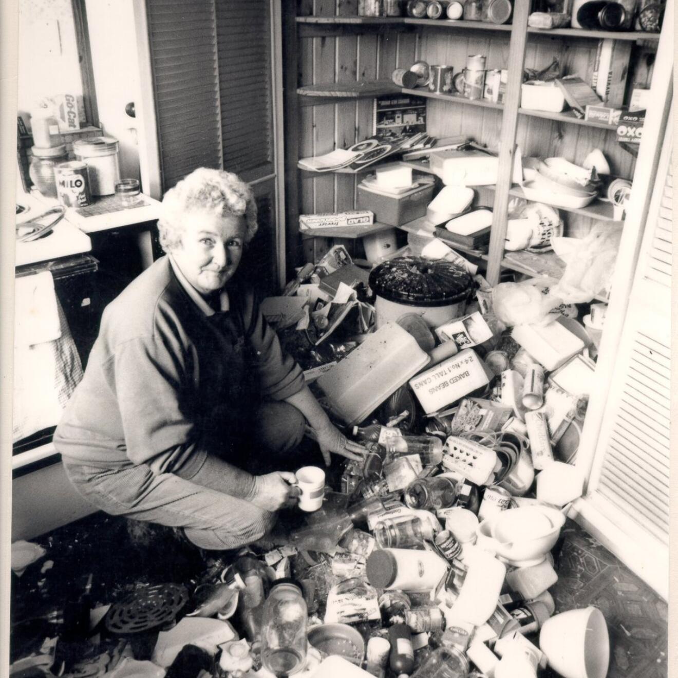 Woman kneeling in kitchen with cupboard contents emptied during 2007 earthquake