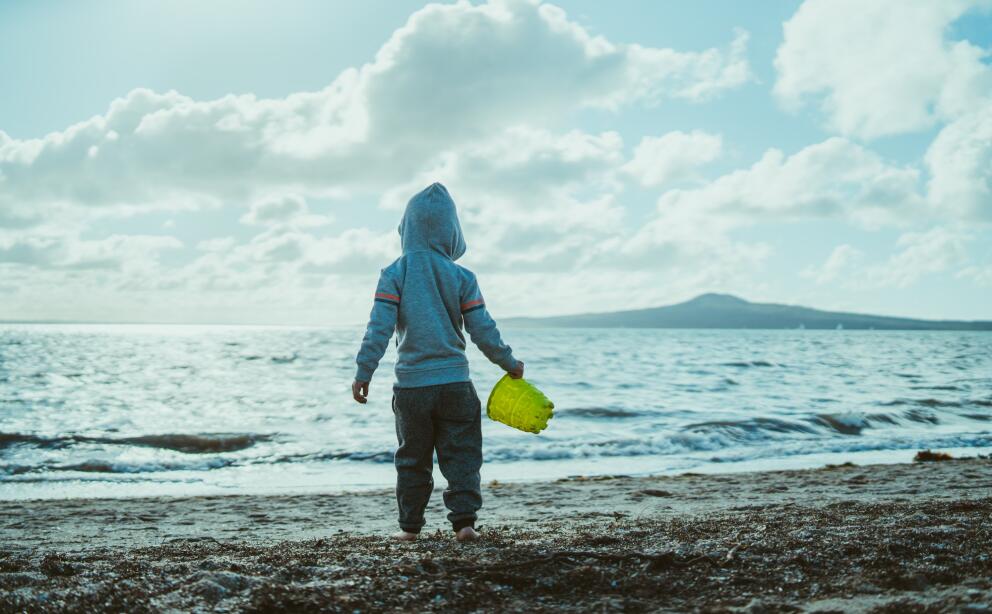 Child standing on a beach looking toward Rangitoto Island
